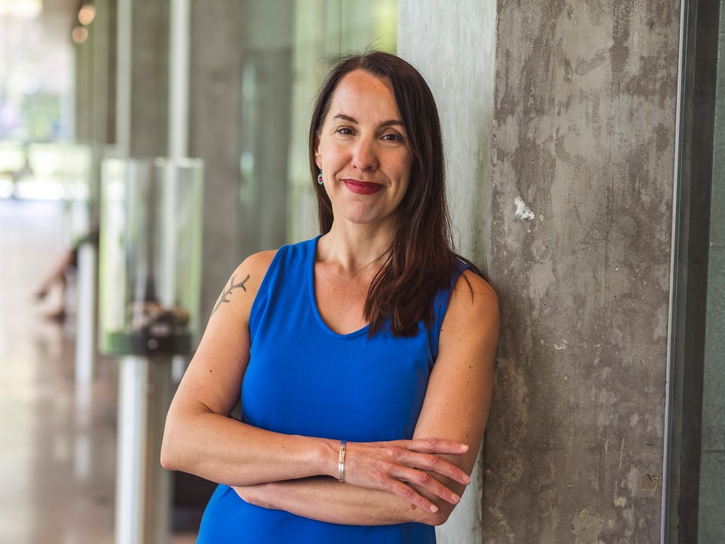 A portrait of Dr. Lyana Patrick leaning against a wall smiling confidently at the camera.