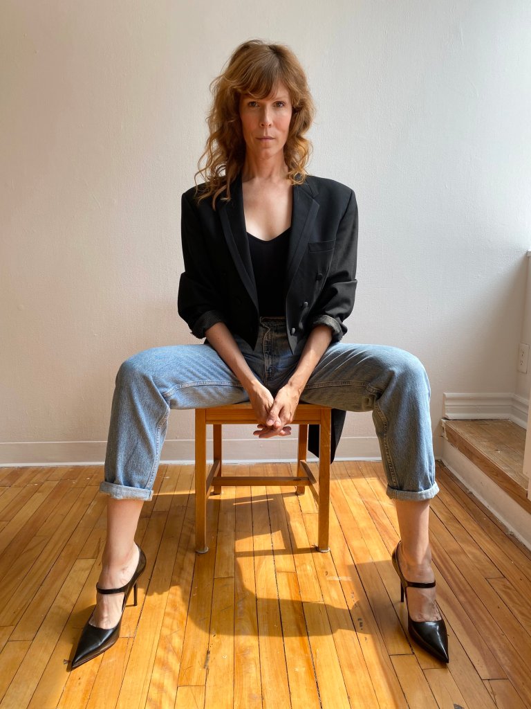 Jordan King, portrait. Jordan sits in a striking pose staring down the camera in fabulous black heels.